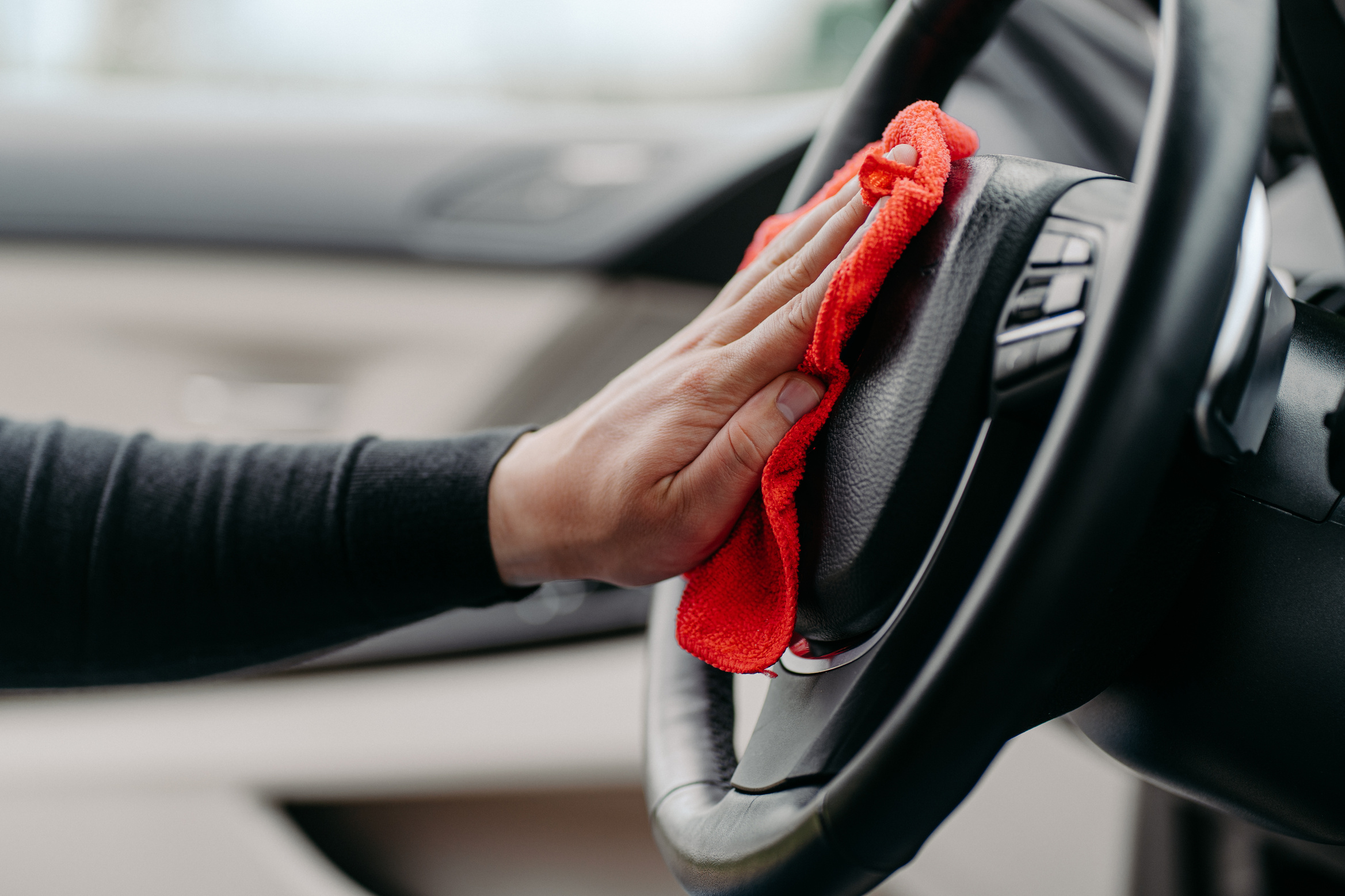 Image gros plan sur une main tenant un chiffon microfibre rouge pour nettoyer le volant d'une voiture.