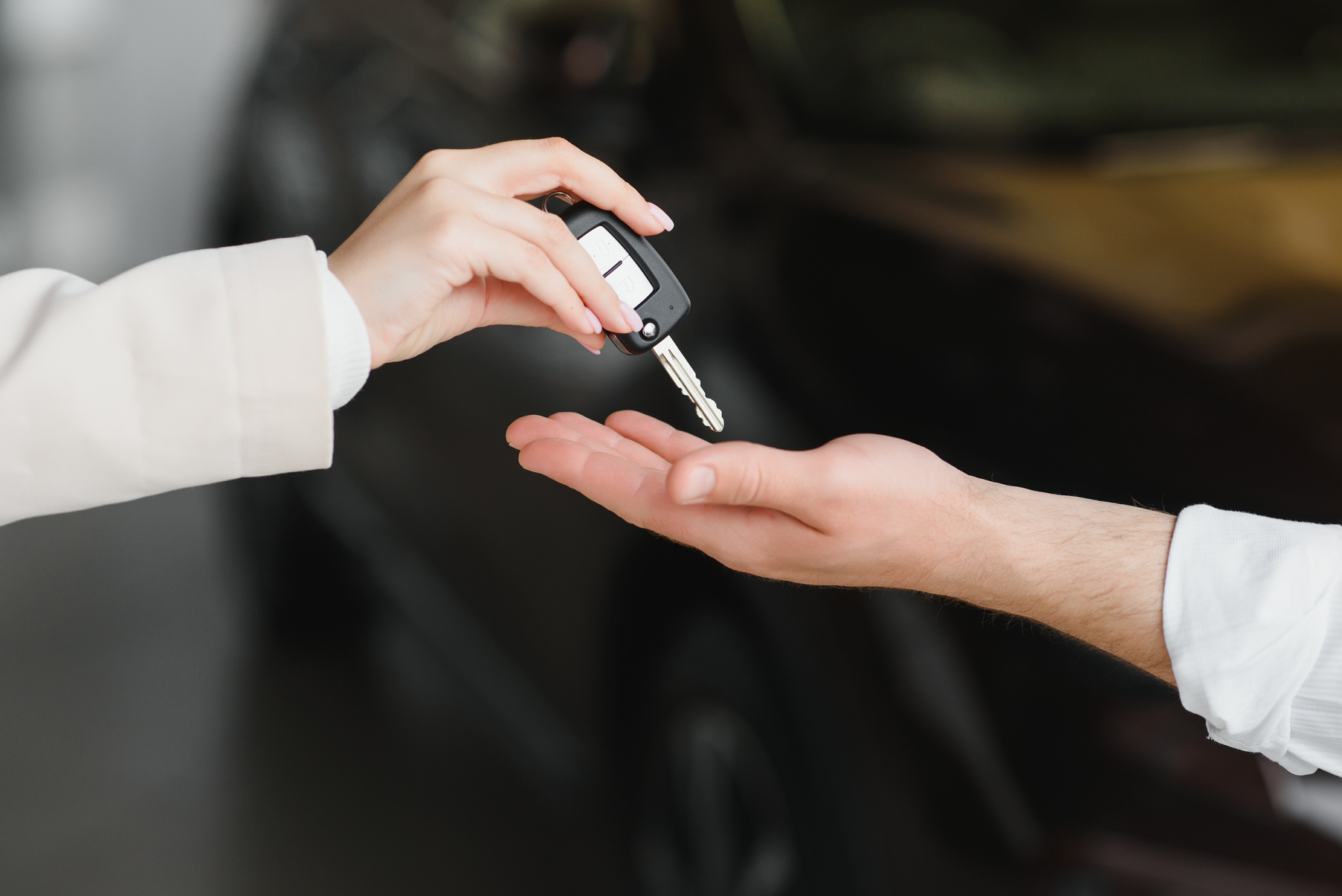 Image gros plan sur une main de femme remettant une clé de voiture noire à une main d'homme.